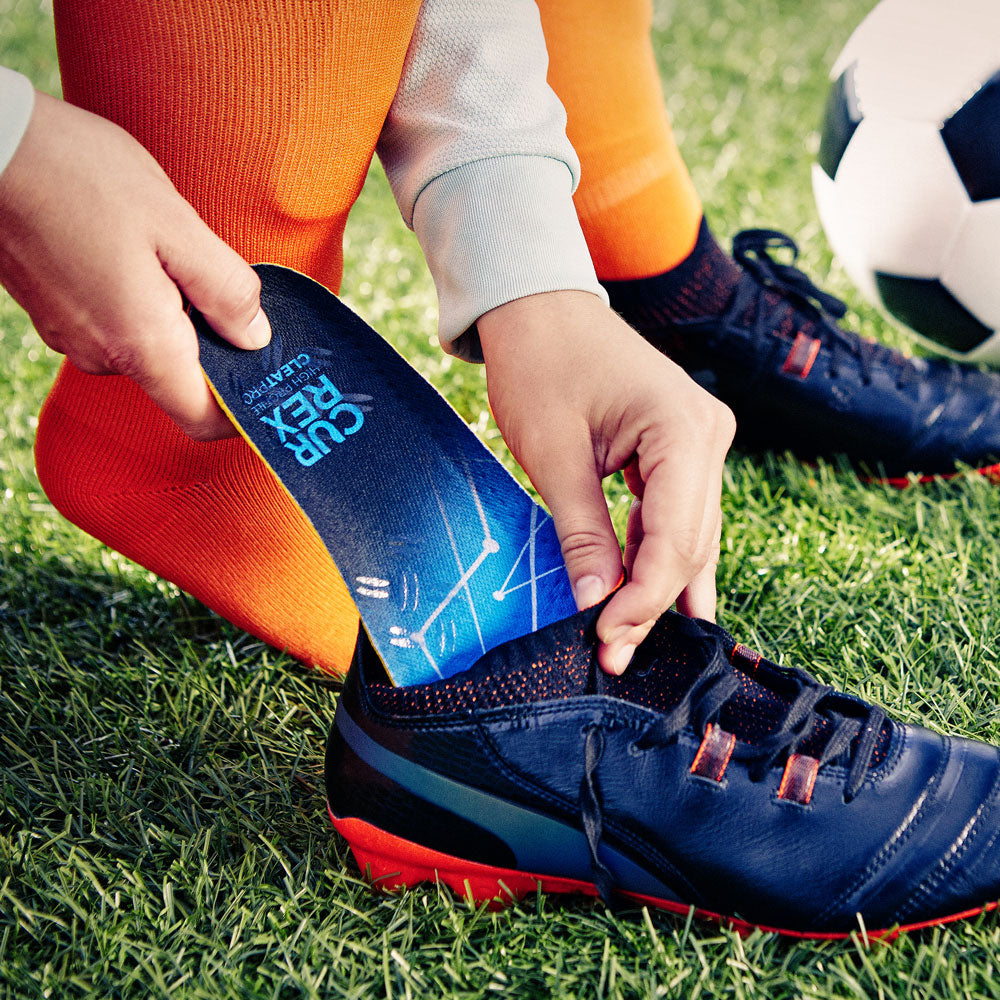 Person placing CURREX CLEATPRO high profile insoles into black cleats on soccer field #1-wahle-dein-profil_low